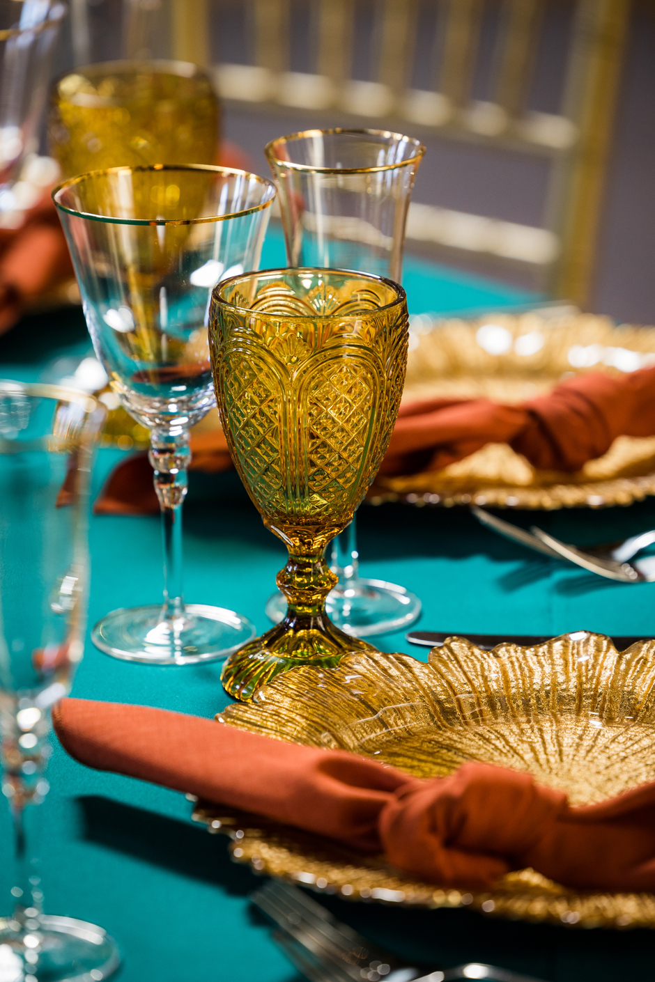 Gold petal charger plate with teal Essential linen, burnt orange Gelato napkin, gold trim glasses & amber goblet