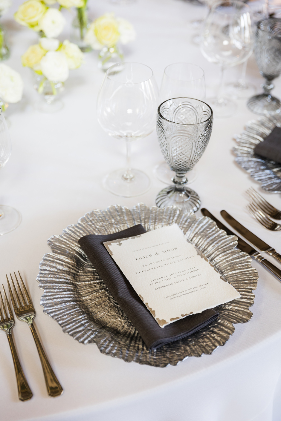 Silver petal charger plate with white Essential linen, graphite Gelato napkin, Riedel glasses & smoke goblet